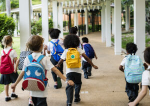 Kindergartens running down hallway with bookbags